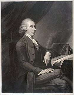 A drawing of an elderly man sitting by a table and facing parallel to the drawing. His left arm rests on a notebook, legs crossed.