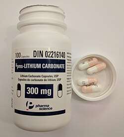 A bottle of lithium carbonate capsules with the cap off. Inside the cap are four lithium carbonate 300 mg pills.