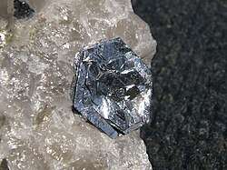 Lustrous, silvery, flat, hexagonal crystals in roughly parallel layers sit flowerlike on a rough, translucent crystalline piece of quartz.