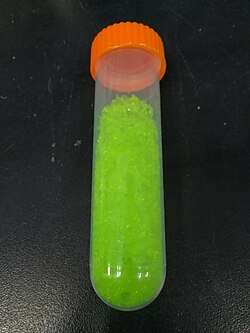 yellowish green crystals in a transparent vial with an orange ribbed screw on cap