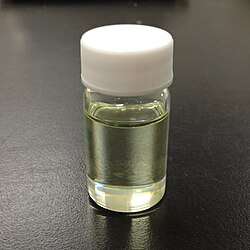 Slightly yellow liquid in a vial with a white cap on a black table