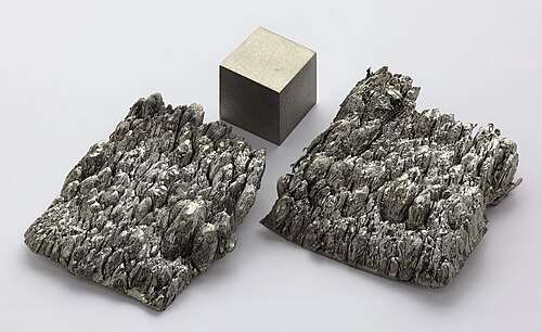 Two samples of rounded dark gray scandium crystals and a metal cube of the same material