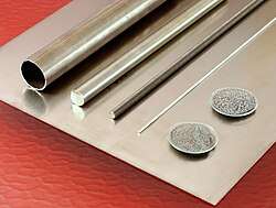 Silvery metal items, including rods, a tube, and powder in plastic containers, all resting on a reflective metal plate