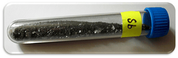 A clear vial containing small chunks of a slightly lustrous black solid, labeled "Sb".