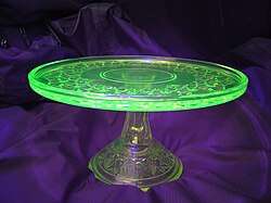 A glass place on a glass stand. The plate is glowing green while the stand is colorless.